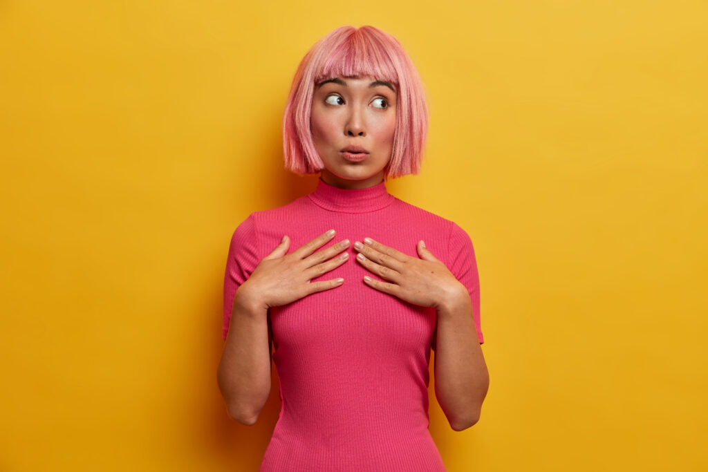 human emotions, reaction and attitude concept. beautiful pink haired young woman keeps hands on chest and looks with wondered expression aside, has suspicion about something, feels skeptical